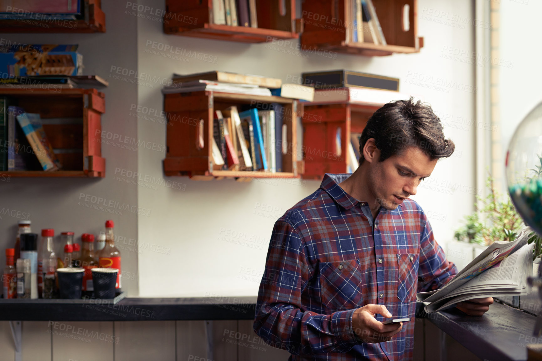 Buy stock photo Man, phone and reading a newspaper at cafe, texting and app for communication at coffee shop. Male person, local news and paper for information at restaurant, headlines article and job search column