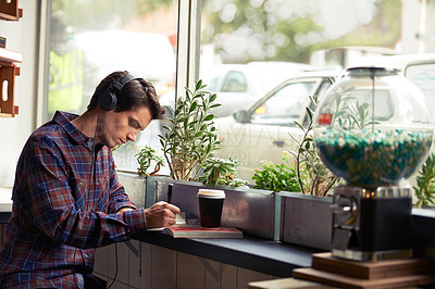 Buy stock photo Shot of a young man studying in a cafe and listening to music 