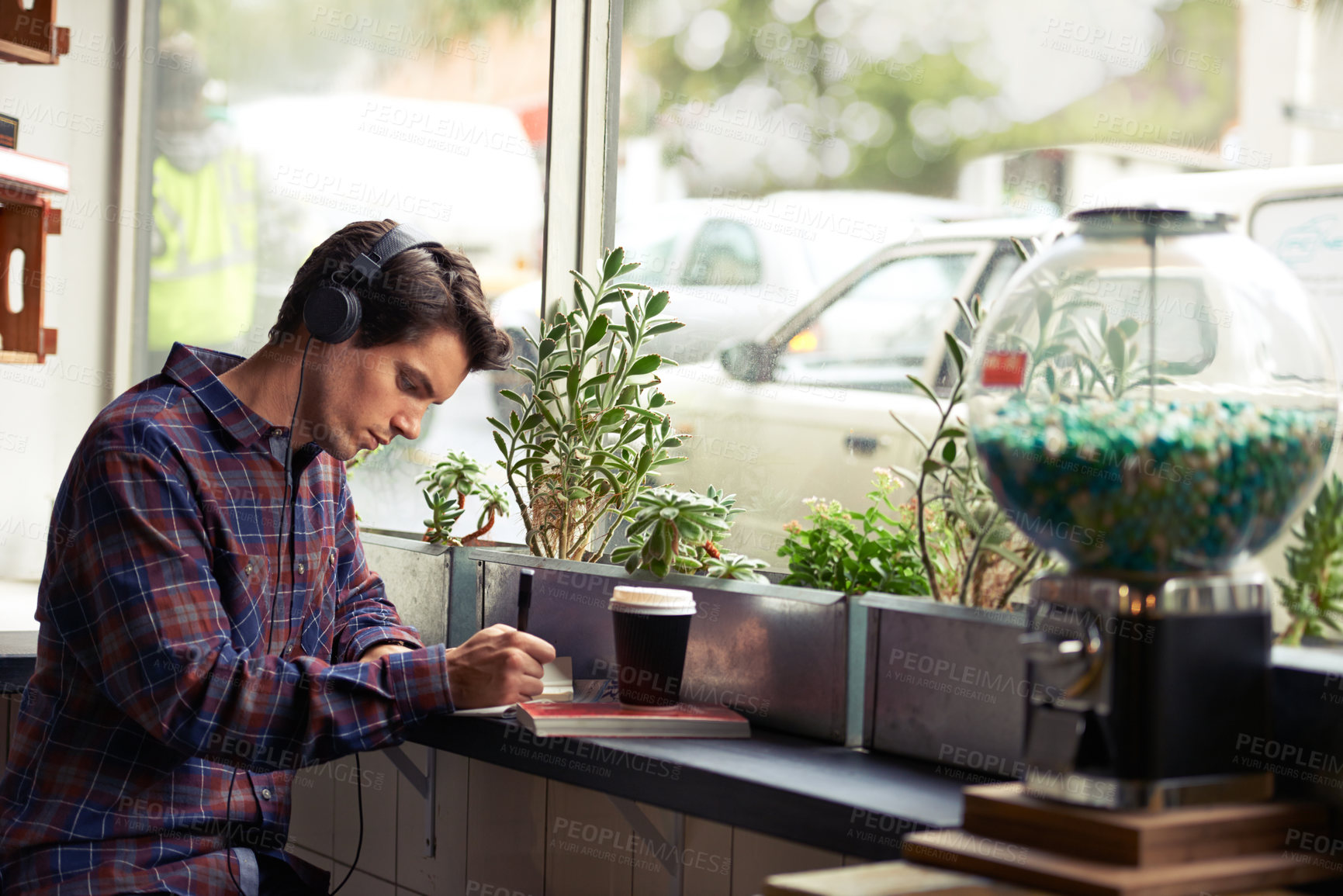 Buy stock photo Shot of a young man studying in a cafe and listening to music 