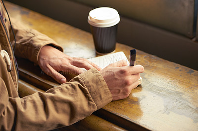 Buy stock photo Man writing in his notebook while sitting in a cafe. Closeup hands of a writer making notes of ideas or thoughts in a diary with a pen while enjoying coffee break. Making a list and planning his day