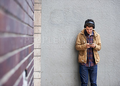 Buy stock photo Texting, headphones and man with phone by wall for communication, connection or chat. Mobile, outdoor or male student in city on urban street for music app, social media website or news notification