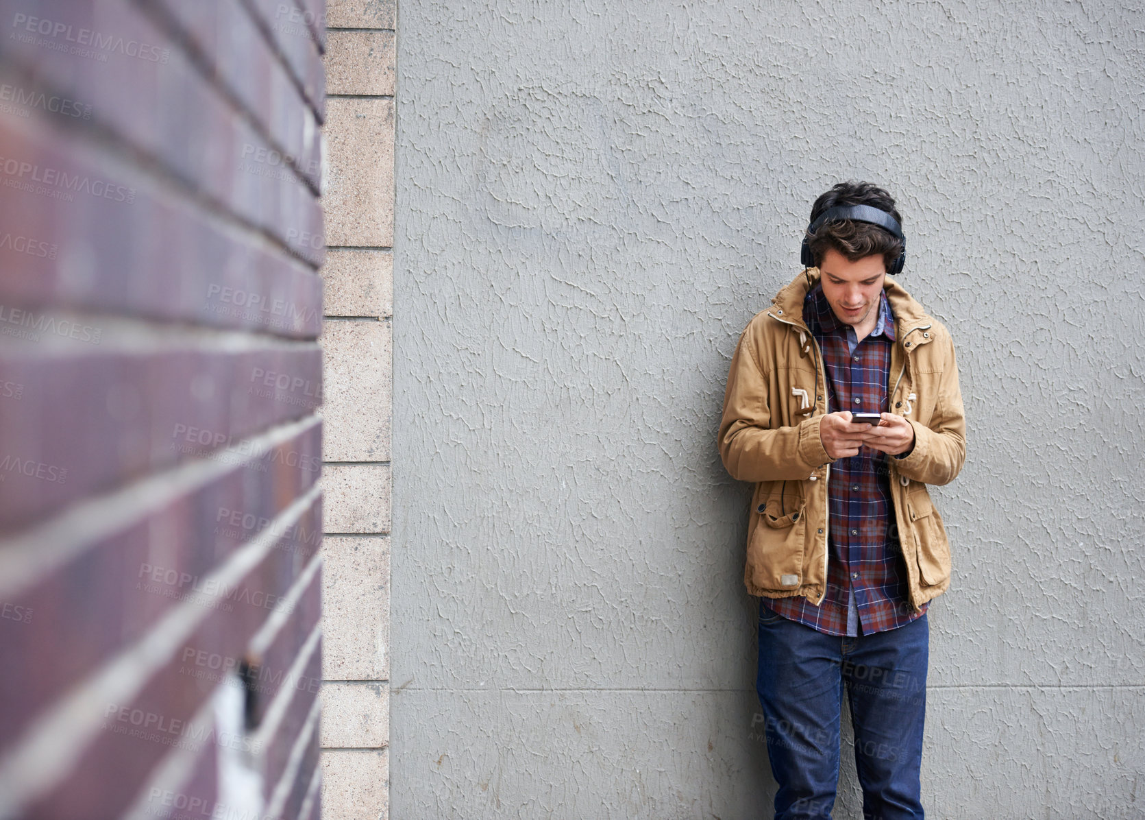 Buy stock photo Texting, headphones and man with phone by wall for communication, connection or chat. Mobile, outdoor or male student in city on urban street for music app, social media website or news notification