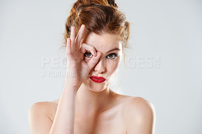 Buy stock photo Portrait of a redhead posing topless and looking through fingers symbolizing glasses, goggles, binoculars or vision. Headshot of a beautiful young woman isolated against a grey background in studio