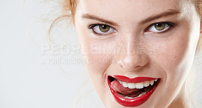 Buy stock photo Portrait of a beautiful woman wearing makeup isolated against a grey background in studio. A sexy redhead wearing red lipstick and biting her tongue. Face of a flirty woman licking her lips