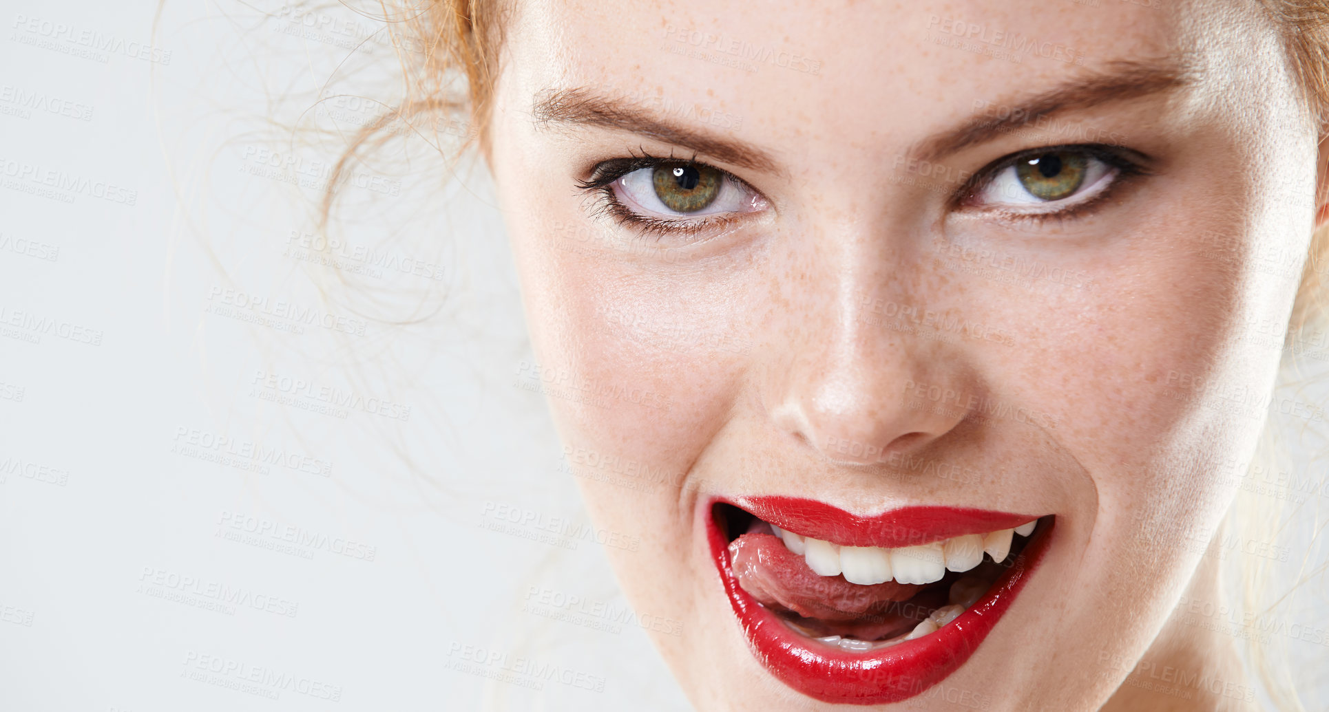 Buy stock photo Portrait of a beautiful woman wearing makeup isolated against a grey background in studio. A sexy redhead wearing red lipstick and biting her tongue. Face of a flirty woman licking her lips