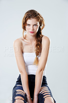Buy stock photo Studio portrait of a Trendy edgy young woman with attitude and braided hair sitting on a chair against a gray background. Beautiful stylish redhead model wearing a white shirt with black ripped jeans
