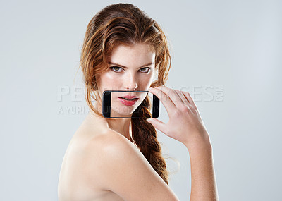 Buy stock photo Studio shot of a young woman holding a mobile phone with a transparent screen in front of her mouth