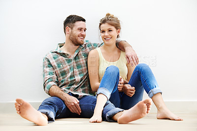 Buy stock photo Shot of a loving young couple sitting beside each other on the floor at home