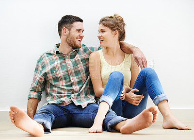 Buy stock photo Shot of an affectionate young couple sitting beside each other on the floor at home