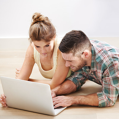 Buy stock photo Shot of a loving young couple using a laptop while lying on the floor at home