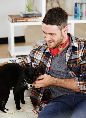 Buy stock photo Smile, man and playing with cat on sofa for pet bonding, headphones or love of animal companion in morning. Happy, male person and relax with kitten friend for fun together, support and care at house