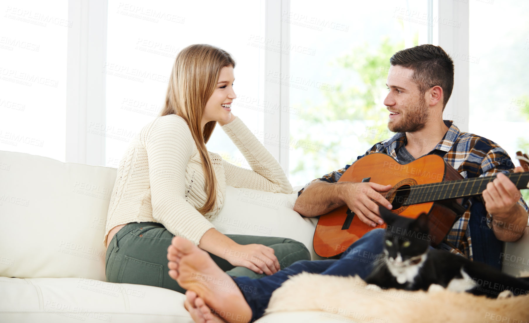 Buy stock photo Shot of a young man playing the guitar for his girlfriend while sitting on their sofa