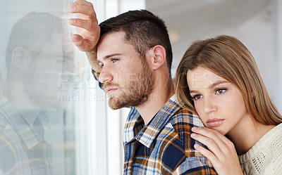 Buy stock photo Shot of a pensive-looking young couple looking out of a window together