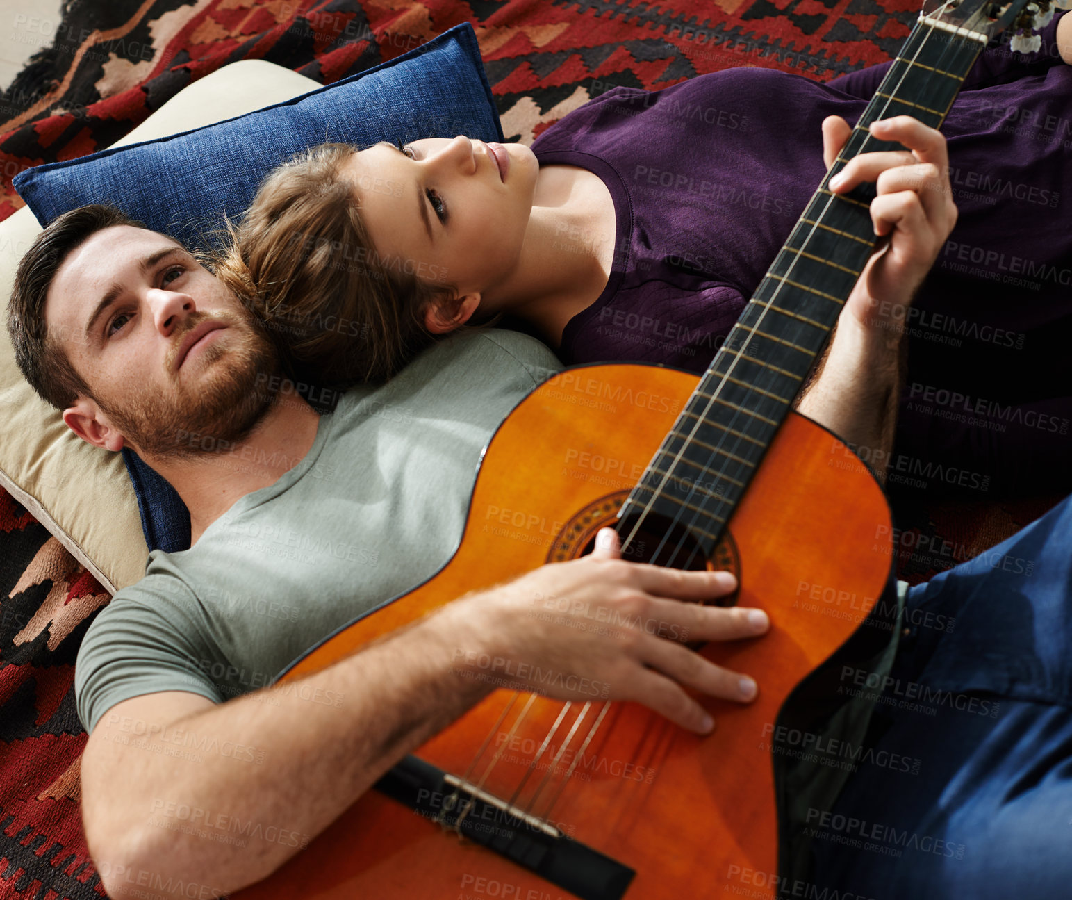 Buy stock photo Shot of a young man playing guitar while lying on the floor with his girlfriend