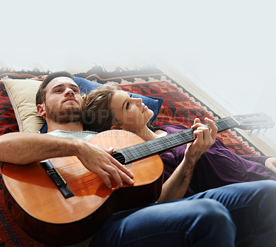 Buy stock photo Shot of a young man playing guitar while lying on the floor with his girlfriend
