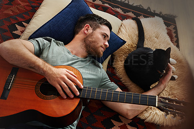 Buy stock photo Single male playing acoustic guitar and bonding with his pet cat while relaxing at home and enjoying free time. Closeup of young man with a guitar lying on the floor and petting his cat, from above. 