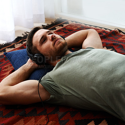 Buy stock photo Young man contemplating decisions while listening to a podcast. Closeup of a young man lying on the floor listening to music wearing headphones and a pillow behind his head looking thoughtful