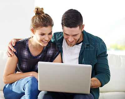 Buy stock photo Shot of a happy young couple using a laptop while relaxing at home together