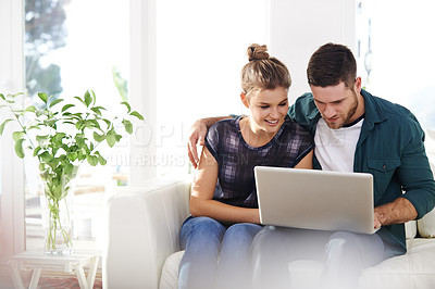 Buy stock photo Shot of a happy young couple using a laptop while relaxing at home together