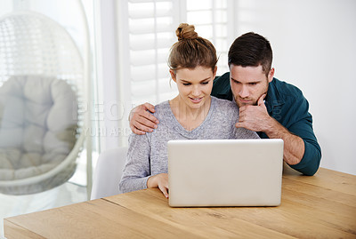 Buy stock photo Shot of a happy young couple using a laptop while relaxing at home together