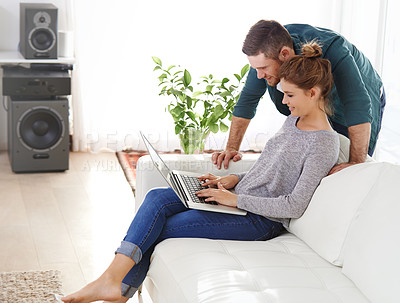 Buy stock photo Shot of a happy young couple using a laptop while relaxing at home together