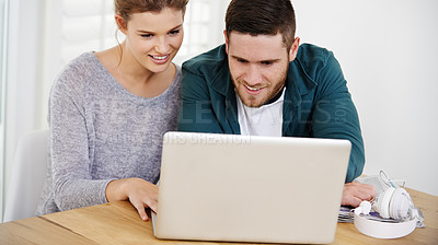 Buy stock photo Shot of a smiling young couple using a laptop while relaxing at home together