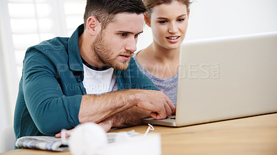 Buy stock photo Shot of a young couple using a laptop while relaxing at home together