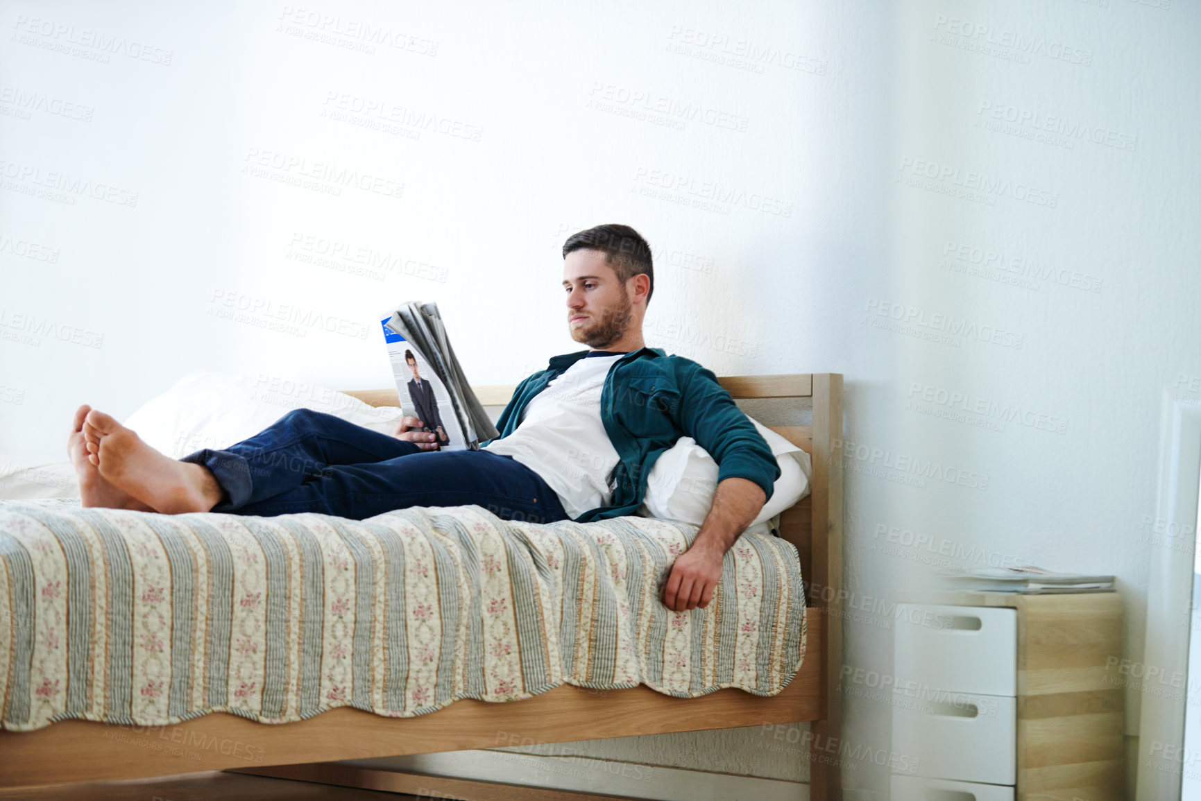 Buy stock photo Man lying on his bed reading a magazine in an apartment. One male enjoying latest issue of a business magazine publication catching up on current news, interests, fashion trends, stock market updates