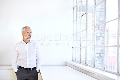 Buy stock photo A mature businessman looking out a window while standing with his hands in his pockets