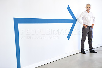 Buy stock photo A mature businessman standing against a white background with a large blue arrow pointing at him
