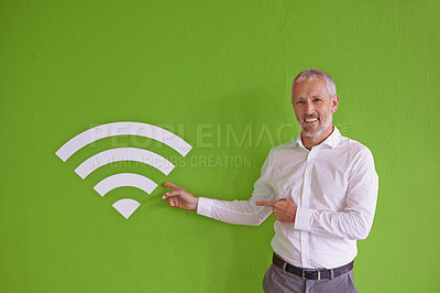 Buy stock photo Portrait of a mature businessman pointing at the wifi symbol next to him against a green background
