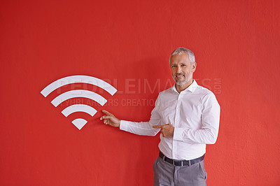 Buy stock photo Portrait of a mature businessman pointing at the wifi symbol next to him against a red background