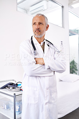 Buy stock photo Shot of a handsome mature doctor looking thoughtful while standing in a hospital room