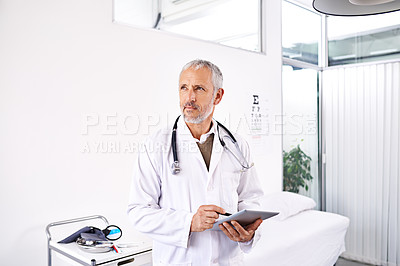 Buy stock photo Shot of a mature male doctor standing with a digital tablet in a medical building
