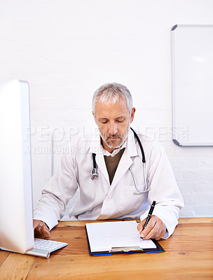 Buy stock photo Shot of a mature male doctor working at a desktop computer in his office