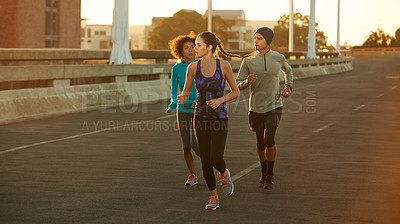 Buy stock photo Shot of a group of friends jogging down a road in the early morning