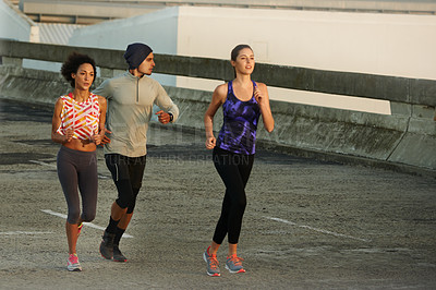 Buy stock photo Shot of three friends jogging together in the city at sunrise