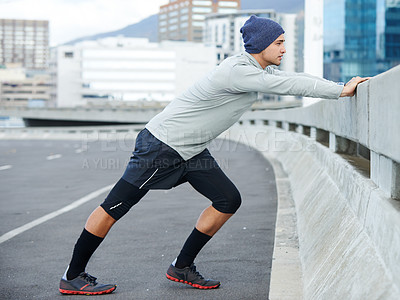 Buy stock photo Shot of a young man stretching before a jog through the quiet city streets