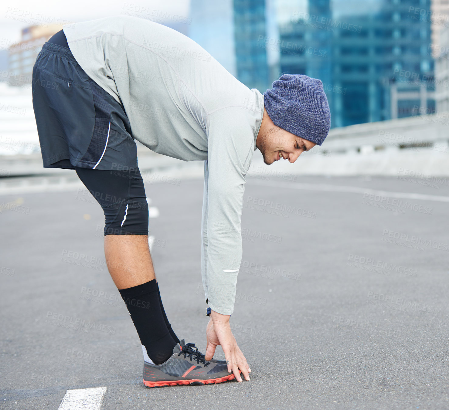 Buy stock photo Shot of a young male jogger stretching in the street before a run