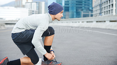 Buy stock photo Shot of a young man tying up his shoelaces before a run through the city