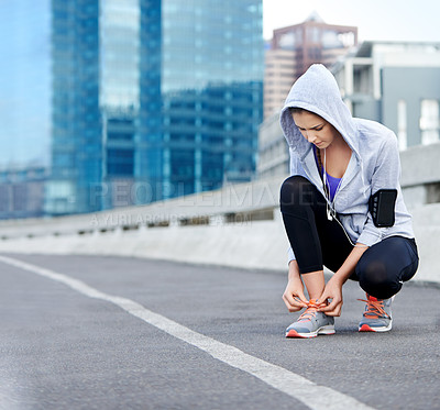 Buy stock photo Shot of a young female jogger tying up her shoes before a run through the city