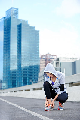 Buy stock photo Shot of a young female jogger tying up her shoes before a run through the city