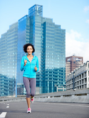 Buy stock photo Shot of a young woman jogging alone through empty city streets