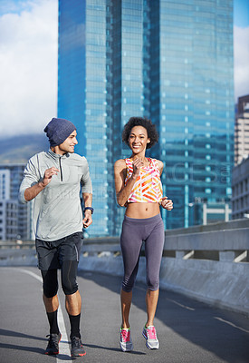 Buy stock photo Shot of two friends jogging together through the city streets