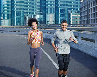 Buy stock photo Shot of two friends jogging together through the city streets