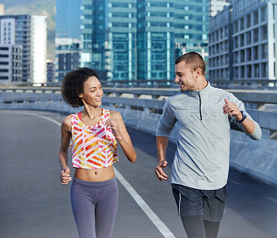 Buy stock photo Shot of two friends jogging together through the city streets