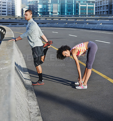 Buy stock photo Shot of two friends stretching together before a run through the city streets