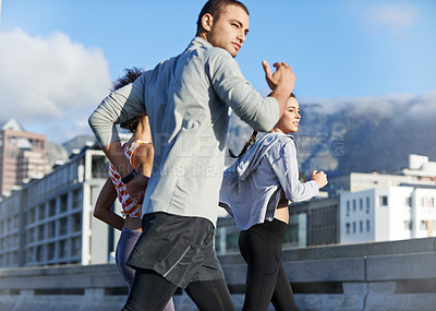 Buy stock photo Shot of a group of friends jogging together through the city