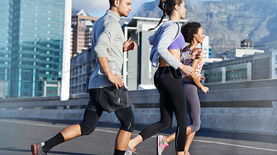 Buy stock photo Shot of a group of friends jogging together through the city