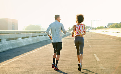 Buy stock photo Rearview shot of two friends jogging through the city